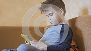 Child watching a movie on mobile phone. Bored boy home alone. Concept of quarantine and self-isolation