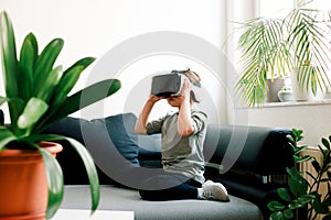 Child watching video or playing game with the help of black-white 3D Virtual Reality glasses sitting on sofa