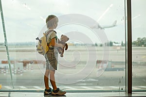 Child, watching from the window of the airport the planes, taking off and landing while waiting at to board the aircraft