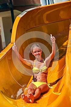 Child on water slide at aquapark show thumb up.