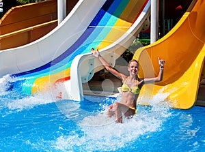 Child on water slide at aquapark show thumb up.
