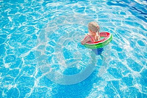 Child with watermelon inflatable ring in swimming pool. Little girl learning to swim in outdoor pool. Water toys and floats for
