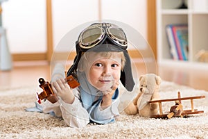 Child weared pilot or aviator plays with a toy airplane at home in nursery room. Concept of dreams and travels.