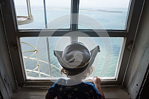 child wearing a captains hat looking out to sea from a high lighthouse window