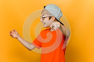 Child wearing glasses for watching movies looks to the side and points his finger forward and mocks photo