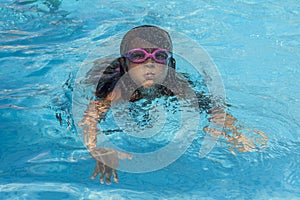 Child wearing goggles, breathing while swimming in the pool.