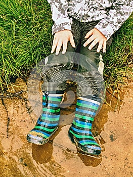 Child wearing rain boots , sits at muddy puddle photo