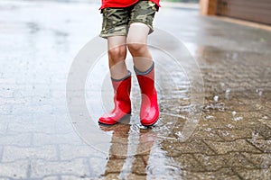 Child wearing red rain boots jumping into a puddle.