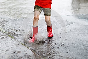 Child wearing red rain boots jumping into a puddle.