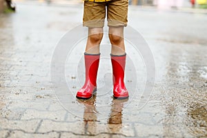 Child wearing red rain boots jumping into a puddle.