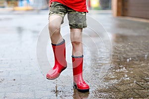 Child wearing red rain boots jumping into a puddle.