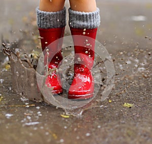 Child wearing red rain boots jumping into a puddle