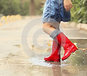 Child wearing red rain boots jumping into a puddle