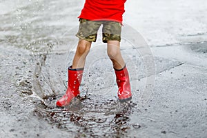 Child wearing red rain boots jumping into a puddle.