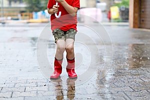 Child wearing red rain boots jumping into a puddle. Close up. Kid having fun with splashing with water. Warm heavy