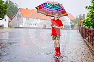 Child wearing red rain boots jumping into a puddle. Close up. Kid having fun with splashing with water. Warm heavy