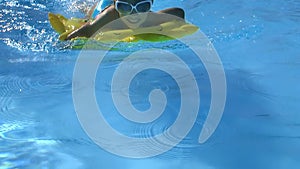 Child wearing sunglasses floating on inflatable ring are swimming in pool.