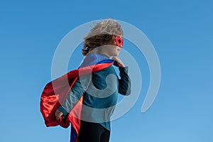 Child wearing a superhero costume. Super hero child against blue summer sky background. Kid having fun outdoors. Kids