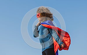 Child wearing a superhero costume. Super hero child against blue summer sky background. Kid having fun outdoors. Kids