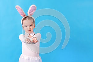 A child wearing a white rabbit. A little girl stretches an Easter egg in her hands. Cute bunny, holiday symbol. Bright