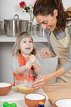 Child whipping to make a cake with mother