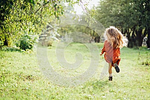 Child whirling, dancing plays on meadow. Girl having fun at nature.