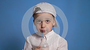 Child in a white shirt and cap drinks kefir from a bottle