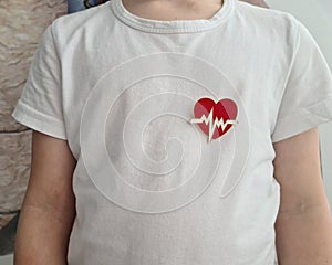 Child in white shirt with heart emblem on chest