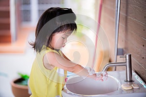Child who loves to be clean is standing washing hands with soap foam in white sink.