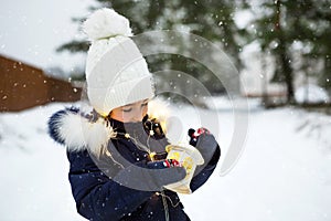 A child in winter on a snowy street under a snowfall in a glowing garland with stars. Preparation for the holiday of Christmas,