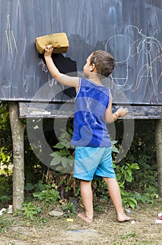 Child wiping blackboard in outdoor classroom