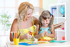 Child with woman cutting out scissors paper in