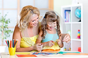 Child with woman cutting out scissors paper in