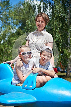 Child and woman fly on blue airplane attraction in city park, happy family, summer vacation concept