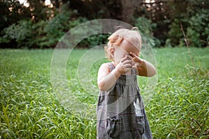 A child in the woods against a backdrop of trees and grass. A one-year-old girl is studying nature. Sunny sunset, a child in a
