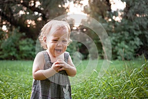 A child in the woods against a backdrop of trees and grass. A one-year-old girl is studying nature. Sunny sunset, a child in a