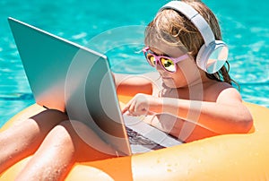 Child working on laptop in summer pool. Little freelancer using computer, remote working in poolside.