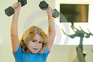Child workout kid in gym. Cute little boy doing exercises with dumbbells. Portrait of sporty child with dumbbells. Happy