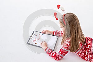 Child writing letter to Santa Claus at Christmas on white background. Top view. notepad for wishes, gift list.Girl in