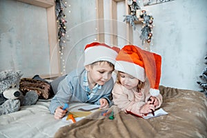 Child writing letter to Santa Claus letter in red hat. Family on Christmas. Bright living room with komin on New Year`s Eve.Cozy