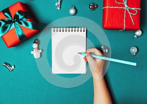 Child writting a letter to Santa. Christmas gift boxes on blue frozen background