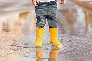 Child& x27;s feet in yellow rubber boots jumping over a puddle in the rain