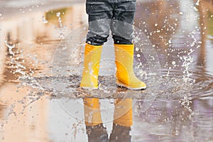 Child& x27;s feet in yellow rubber boots jumping over a puddle in the rain