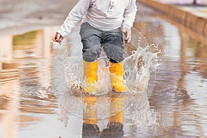 Child& x27;s feet in yellow rubber boots jumping over a puddle in the rain