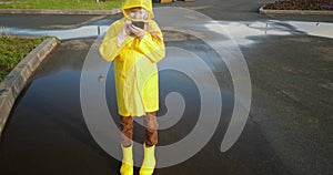 Child in yellow boots stand puddle playing online game in smartphone