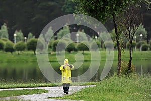 Child in a yellow raincoat alone is in city park