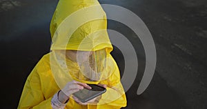 child in yellow raincoat with smartphone play online game outdoors