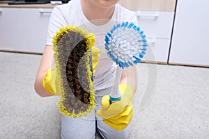 A child in yellow rubber gloves showing bruses for cleaning house, carpet from dust and stains