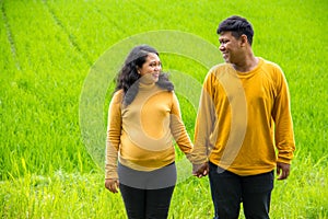 Childbearing couple hold hands and look at each other, over fresh rural country landscape