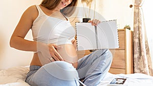 Childbirth checklist pregnant woman. Beautiful pregnancy woman writing check list. Happy pregnant lady holding notepad